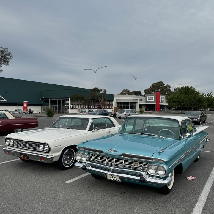 Two classic 1960s American cars, white Chevrolet and turquoise Cadillac, parked in lot