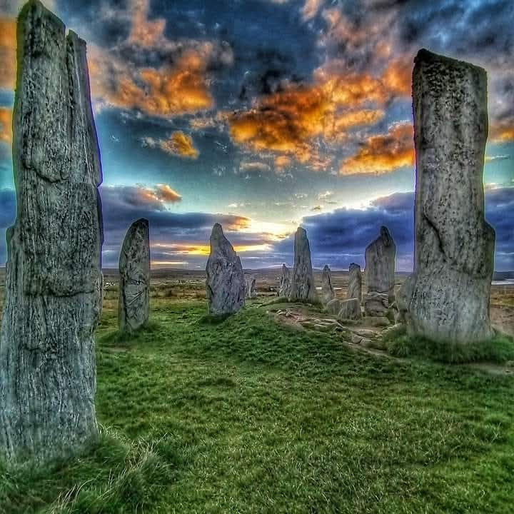 Ancient standing stones in Scotland silhouetted against dramatic orange and blue sunset sky