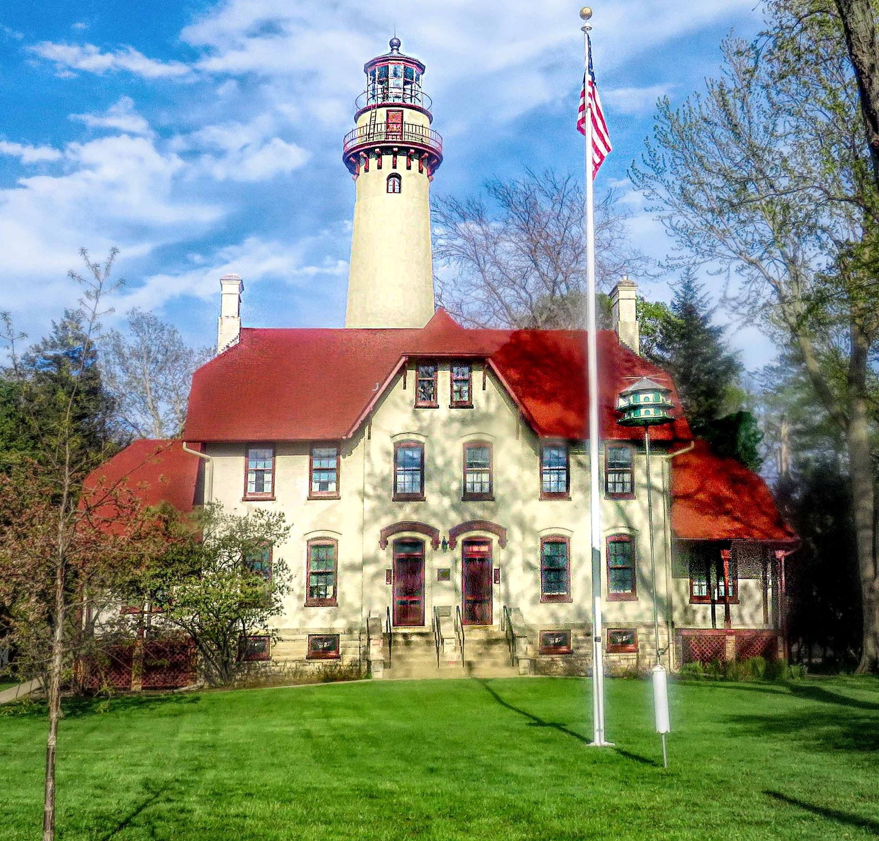 Grosse Point Lighthouse with white tower, red roof, and American flag on sunny day