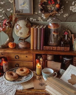 Cozy vintage desk with books, globe, pastries, candle, teacup, and lace cloth