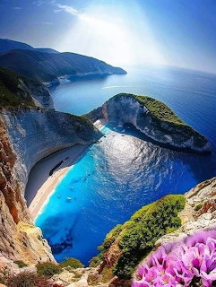 Aerial view of Navagio Beach in Zakynthos with turquoise sea, white cliffs, and pink flowers