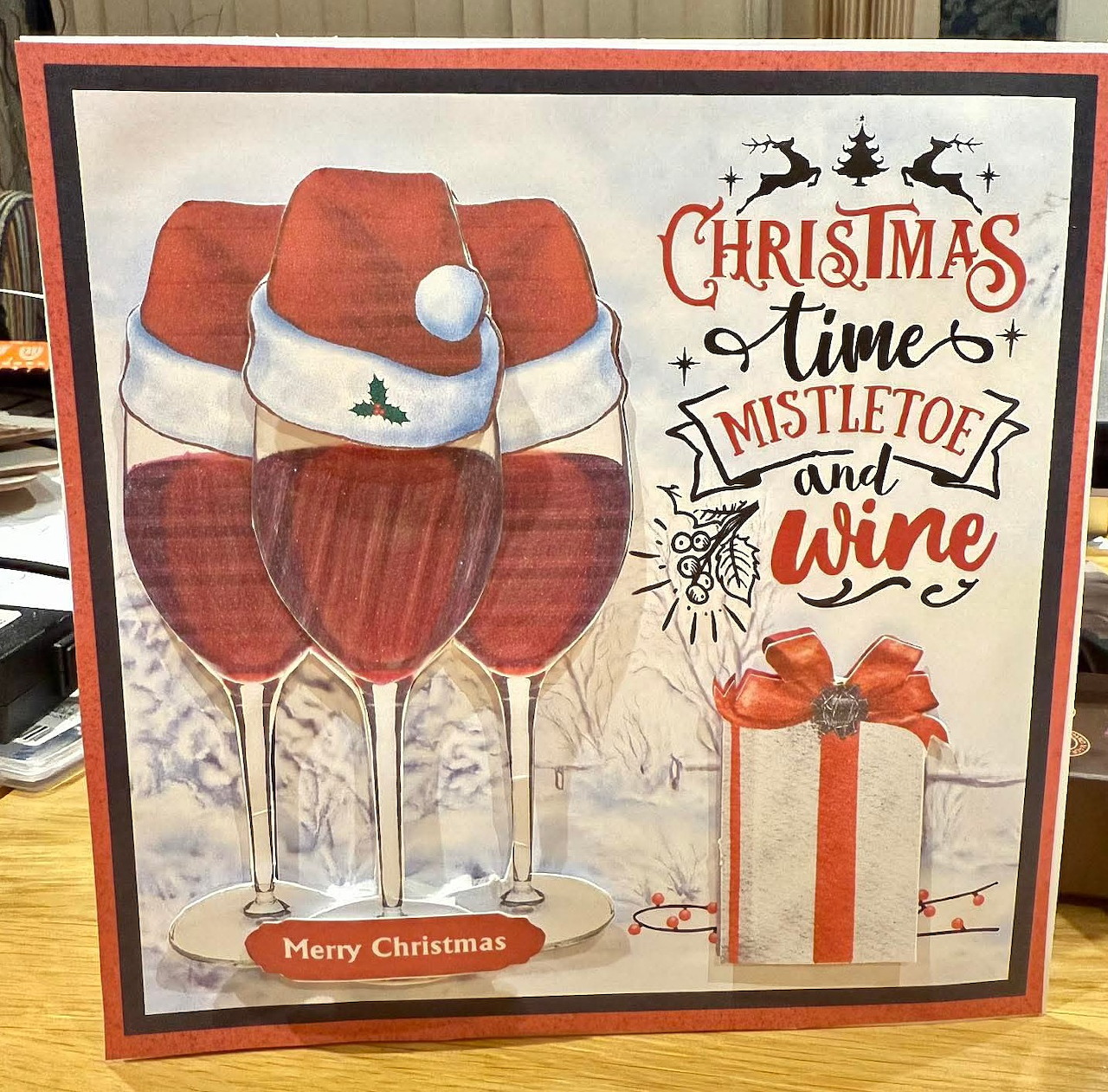 Framed Christmas artwork with wine glasses in Santa hats, festive text, and a gift box