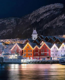 Colorful illuminated wooden buildings along Bergen Norway waterfront at night with mountains behind