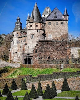 Bürresheim Castle with stone walls, pointed towers, and trimed hedges in the foreground