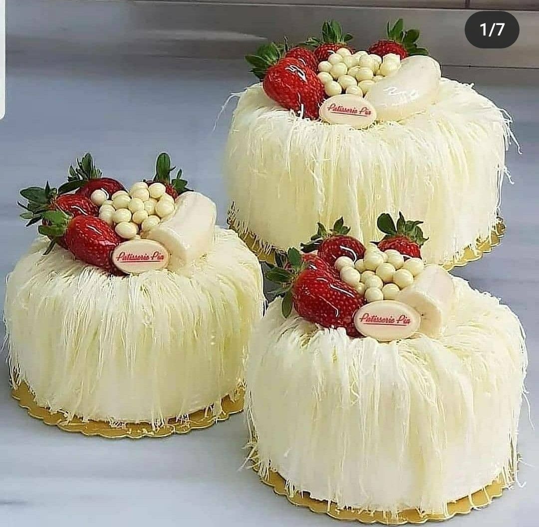 Three small round white coconut cakes topped with strawberries and white chocolate truffles