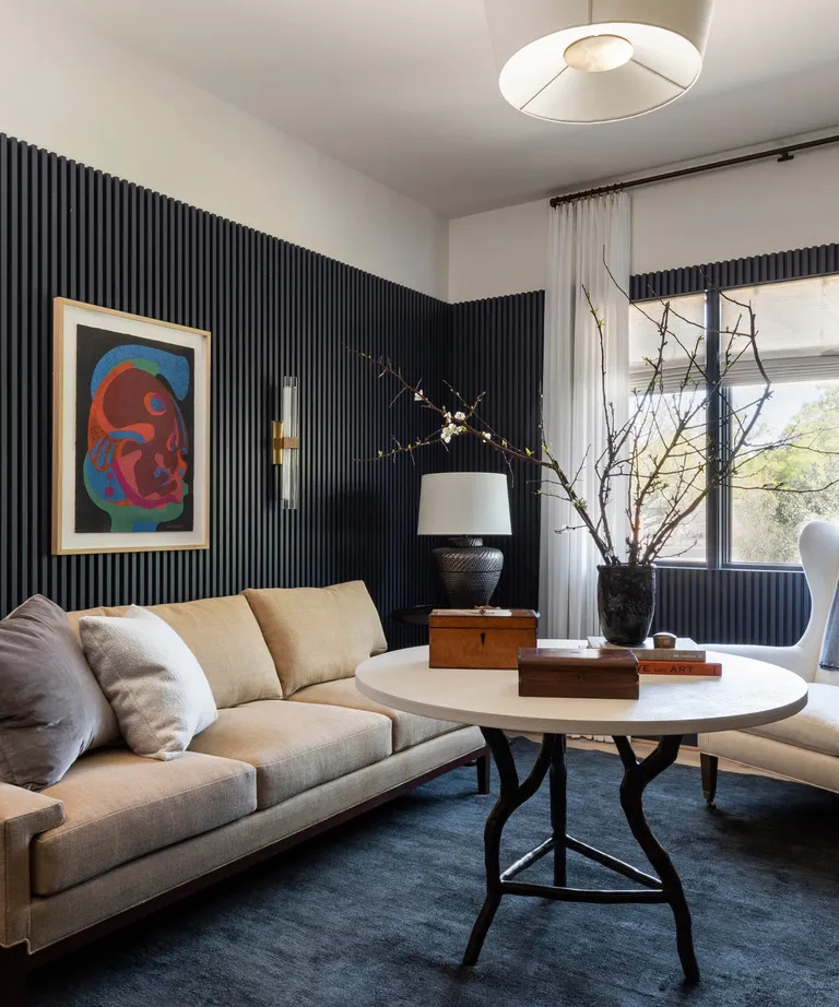 Modern living room with black striped wall, beige sofa, round table, framed art, and window
