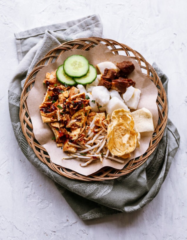 Top-down plate of tahu telor petis with tofu omelet, cucumber, rice cake, bean sprouts, and crackers