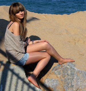 Woman in knit sweater sitting on rock at beach with ocean behind her