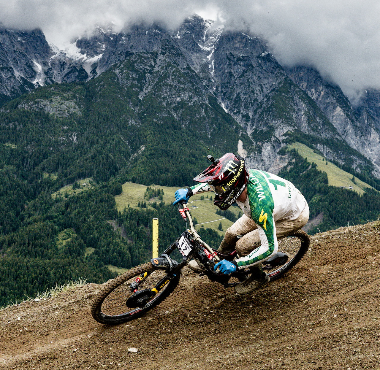 Mountain biker cornering on a dirt trail with alpine mountains behind