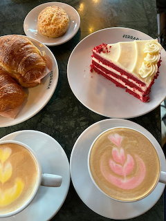 Overhead cafe scene with red velvet cake, croissants, and decorated lattes on marble table