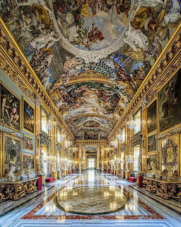 Ornate museum gallery hall with gilded decor, chandeliers, marble floor, and painted vaulted ceiling