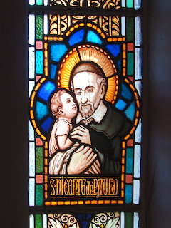 Stained glass church window showing Saint Vincent de Paul holding a baby with a golden halo