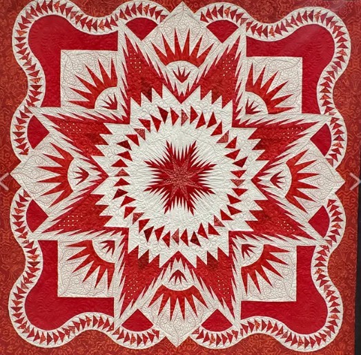 Red and white star quilt with intricate geometric pattern and scalloped border