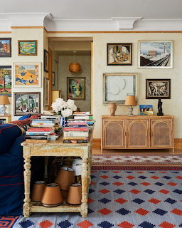 Cozy living room with framed artwork on walls, wooden furniture, patterned rug, and books on coffee table