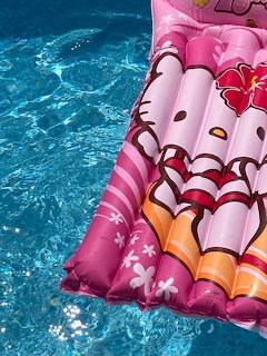 Person on pink Hello Kitty inflatable float in bright blue pool water