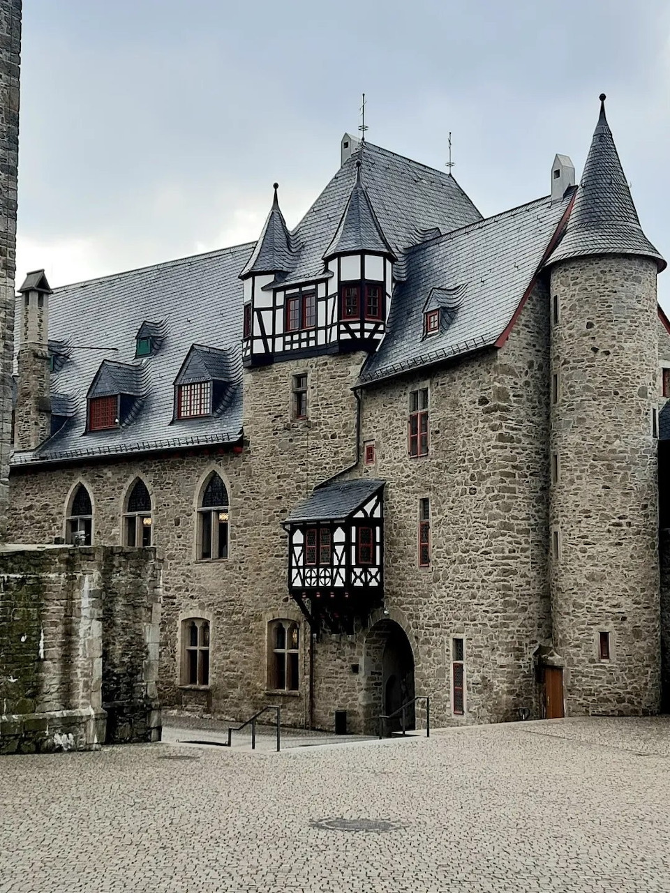 Medieval castle courtyard with stone walls, timber-framed sections, and towers with pointed slate roofs