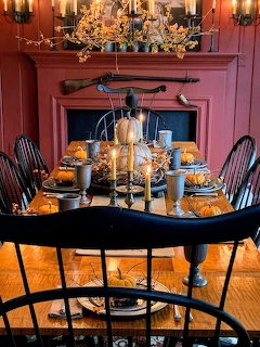 Formal dining room with black table, Windsor chairs, red walls, fireplace, and candlelit table setting