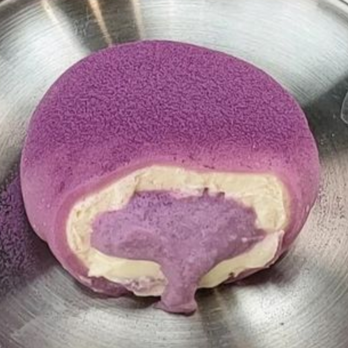 Purple mochi pastry cut open on metal plate revealing cream filling