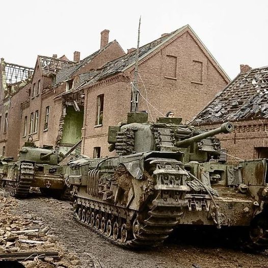 British Churchill tanks on a rubble-covered street beside damaged brick buildings