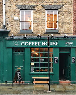 Green-painted Coffee House cafe exterior with brick walls, large windows, and a wooden bench on the sidewalk.