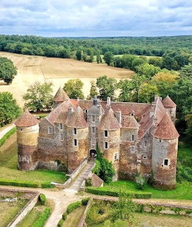 Aerial view of medieval French château with towers surrounded by countryside and fields