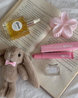 Flatlay of beauty products, stuffed bunny, pink accessories and book on white blanket