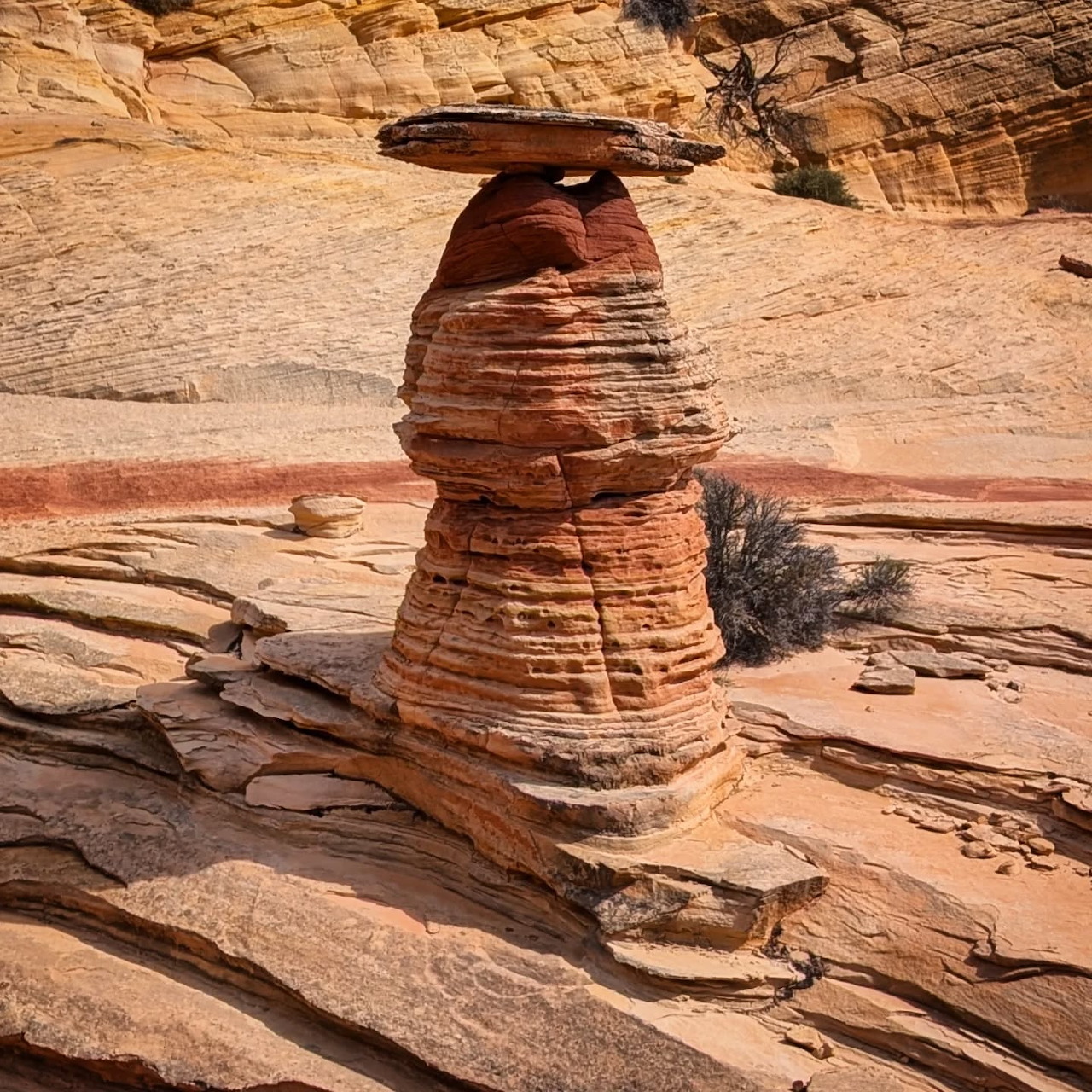 Layered sandstone hoodoo with flat capstone in Utah desert surrounded by eroded rock slabs