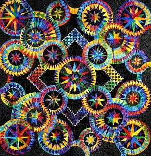 Colorful compass star quilt with radiating geometric patterns in rainbow colors on black background