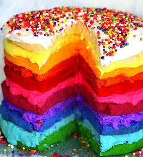 Sliced rainbow layer cake with white frosting and multicolored sprinkles on top