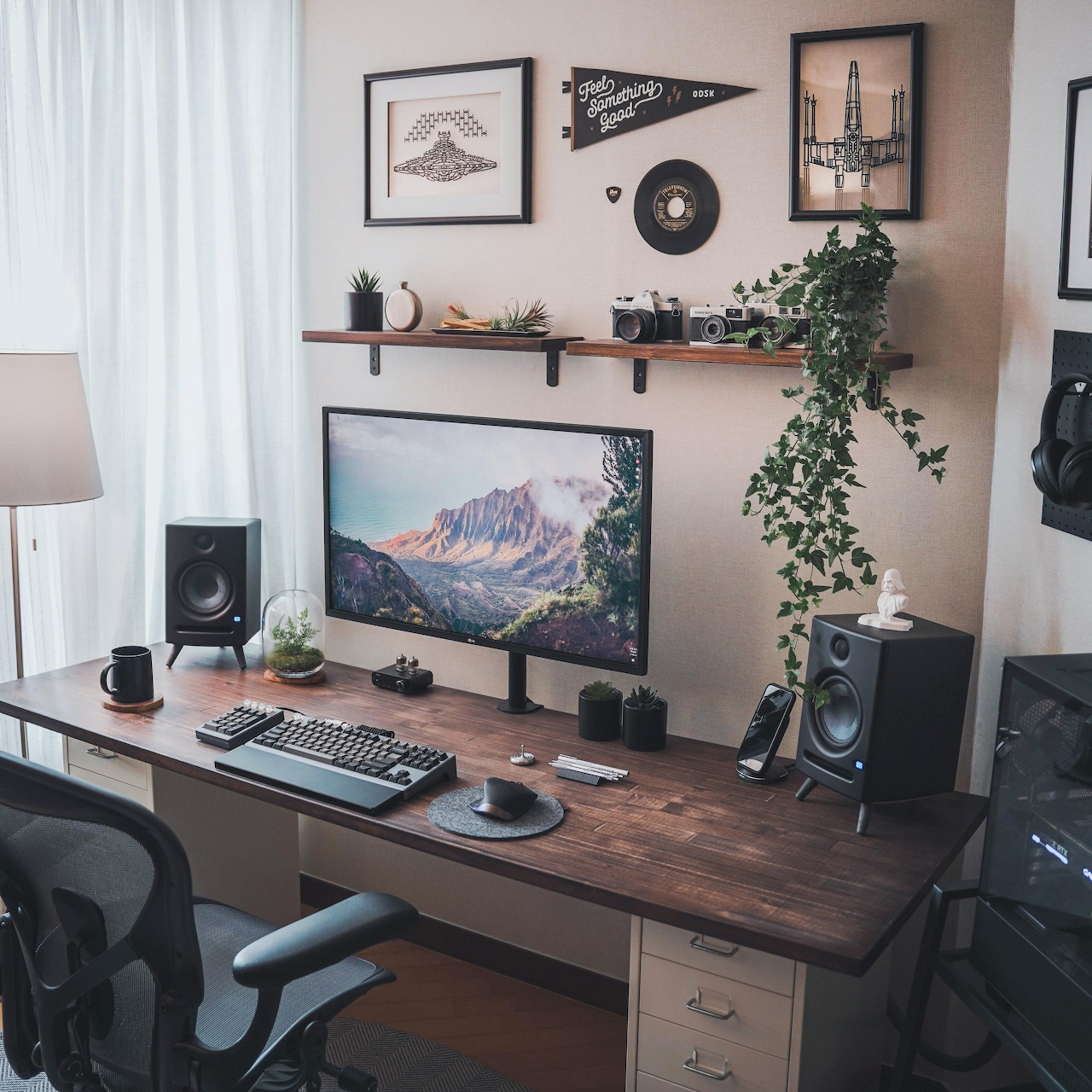 Modern home office desk with computer monitors, speakers, keyboard, and wall decorations with hanging plants