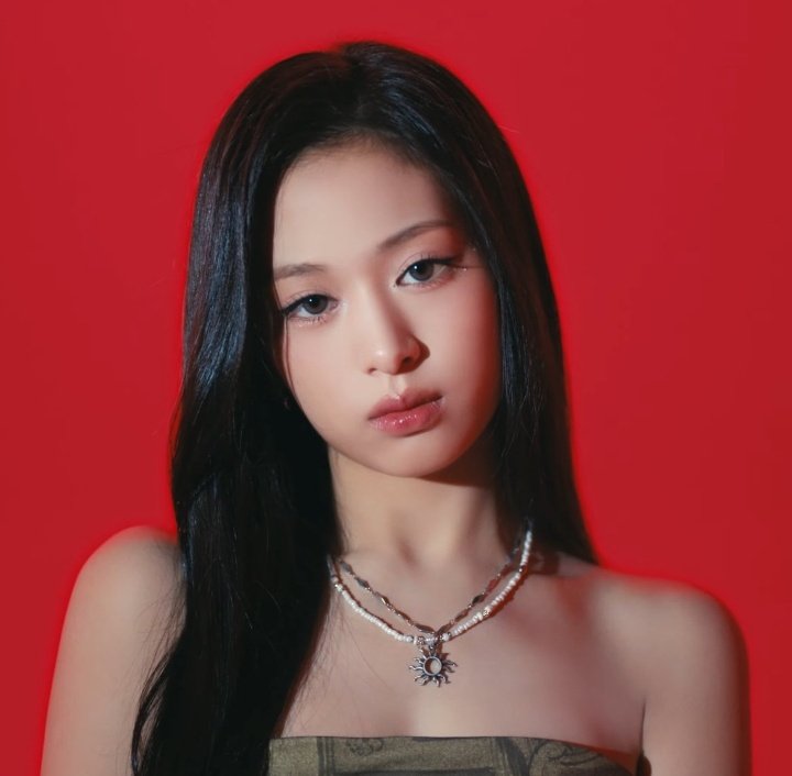 Studio portrait of a young woman with long black hair and layered necklaces against a red background