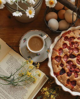 Overhead rustic table with strawberry tart, coffee, open book, eggs, and daisy flowers
