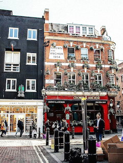 Red brick Crown and Anchor pub on London street corner with pedestrians and bollards