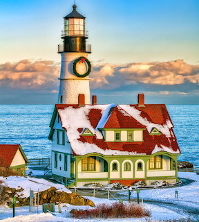 Snow-covered Portland Head Lighthouse with Christmas wreath and red-roofed house by the ocean