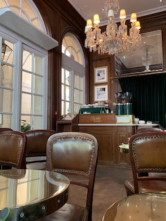 Elegant cafe interior with brown leather chairs, wooden counter, arched windows, and crystal chandeliers