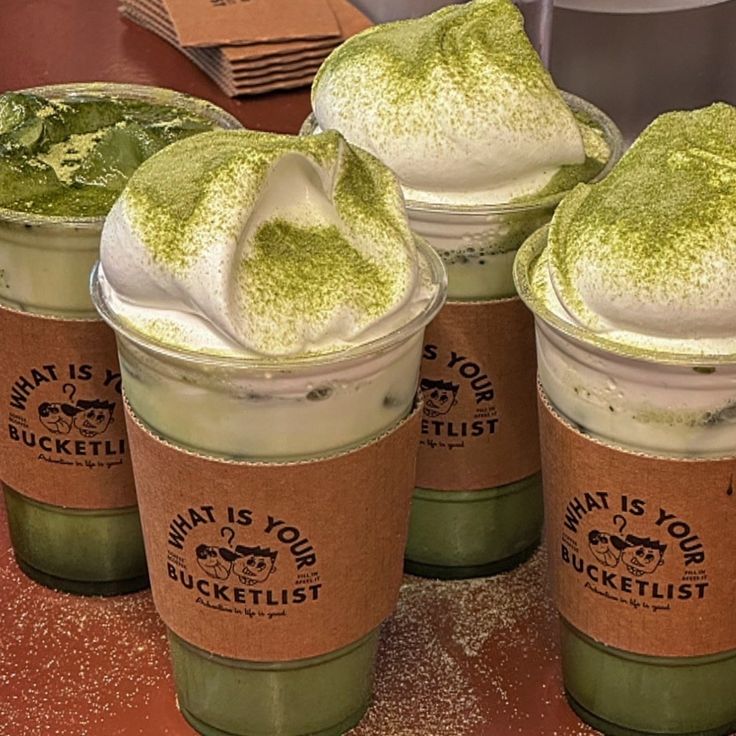 Four iced matcha latte drinks with whipped cream and matcha powder on top