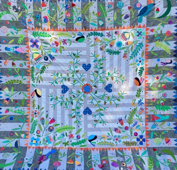 Handmade quilt with floral vines and birds on light blue center, surrounded by colorful patchwork border