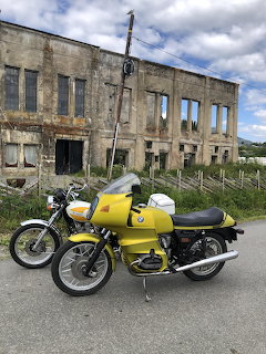 Two vintage yellow motorcycles parked before a derelict building