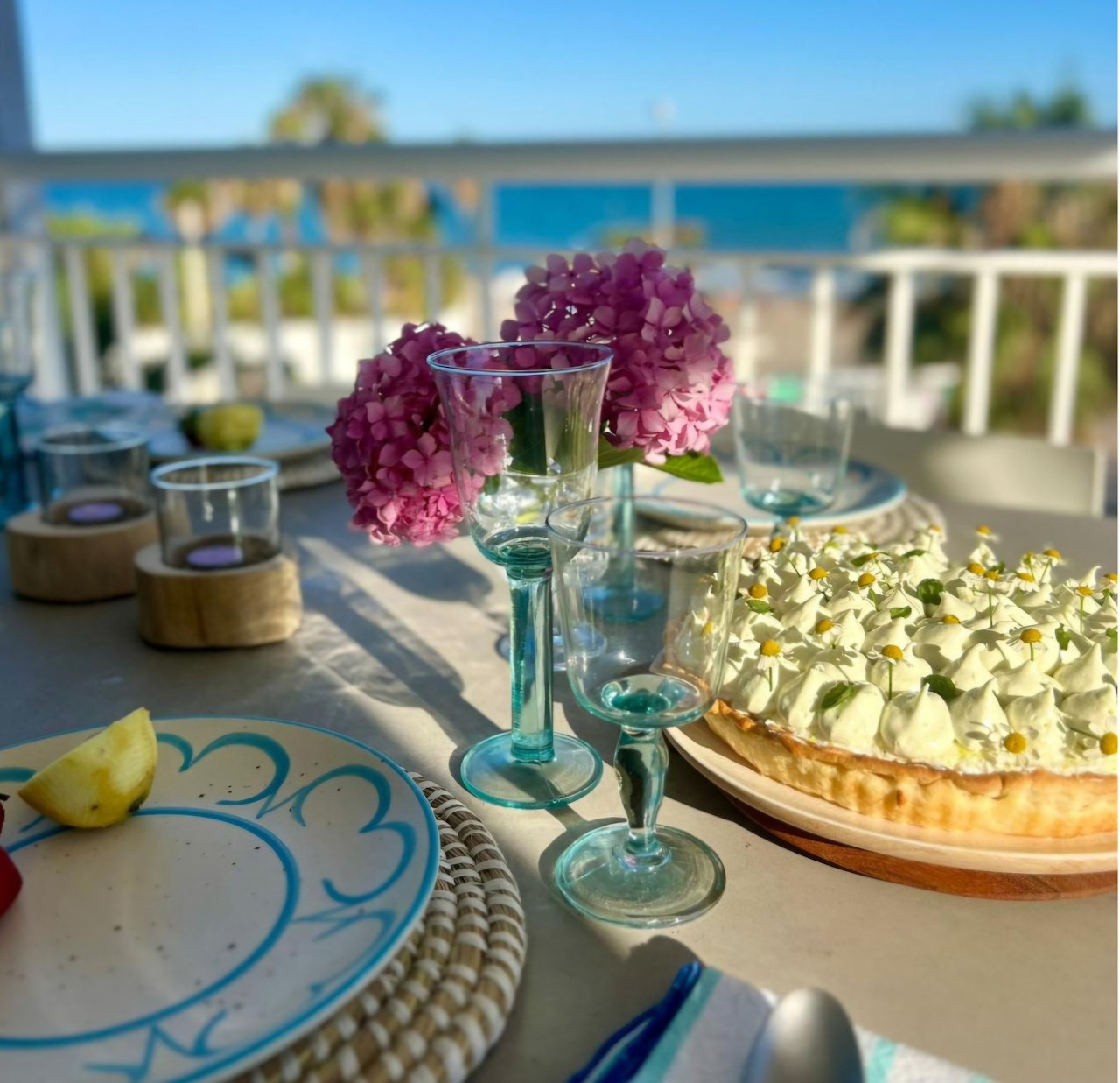 Table with pink hydrangeas, lemon tart, and turquoise vase overlooking ocean