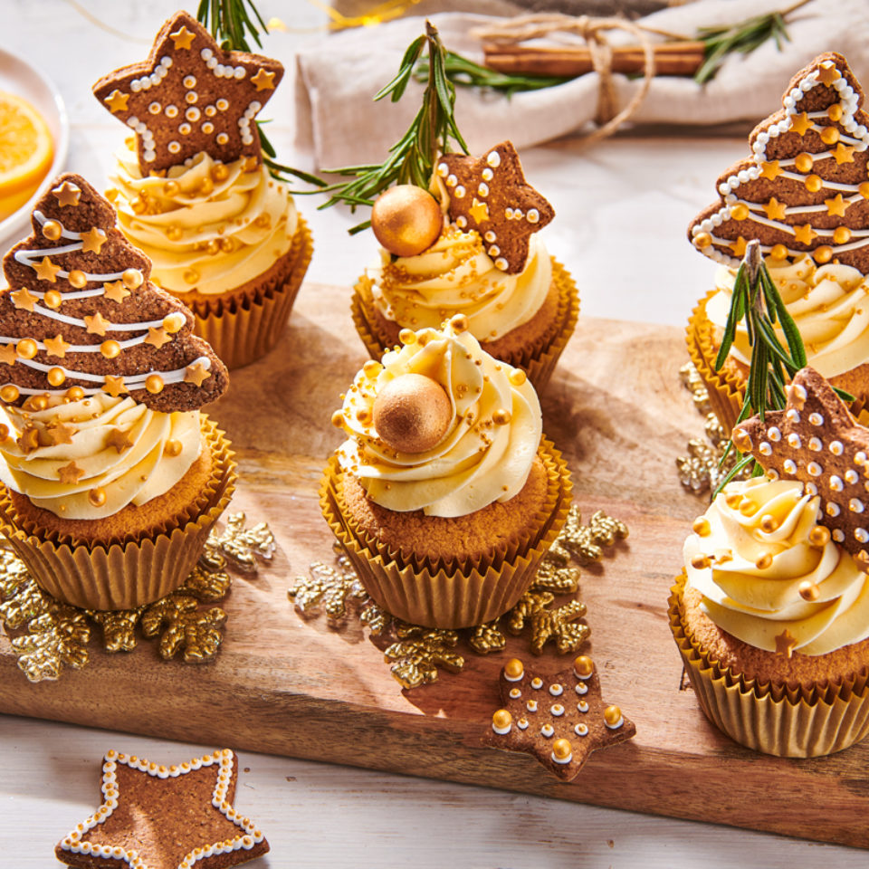 Christmas cupcakes topped with frosting and gingerbread star and tree cookies on a wooden board