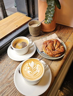Two latte coffees with leaf art beside a flaky pastry on a wooden windowsill