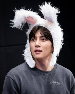 Young man in a fluffy white bunny ear hat and gray shirt against a dark background