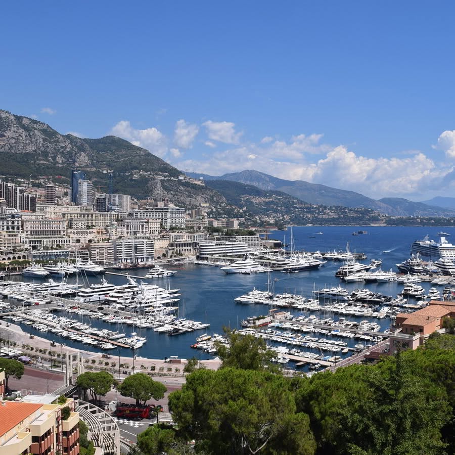 Coastal city marina packed with yachts, backed by mountains and a bright blue sky