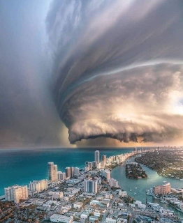 Enormous swirling storm cloud formation over Miami Beach skyline and turquoise ocean from aerial view