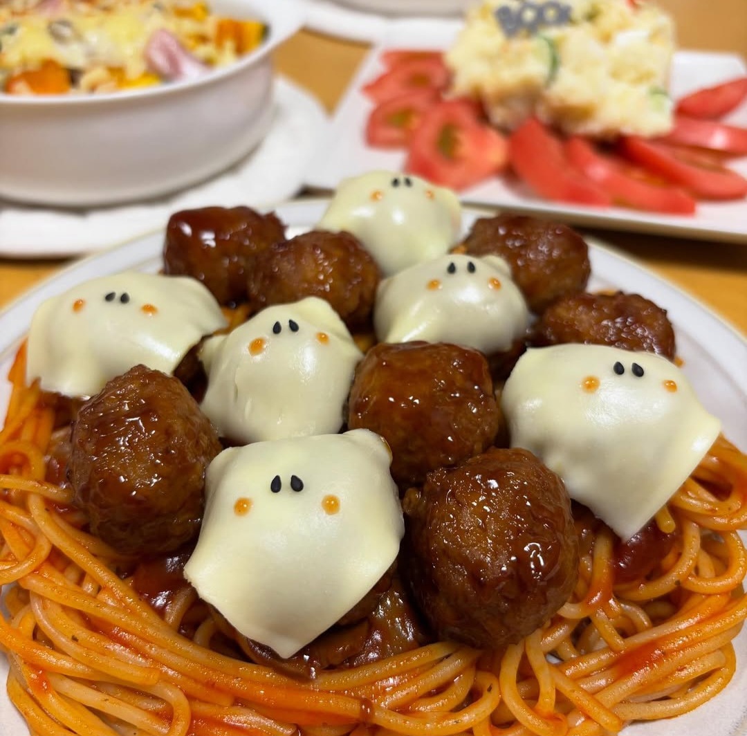 Meatballs topped with ghost-shaped white sauce on orange spaghetti, arranged in rows with cute faces