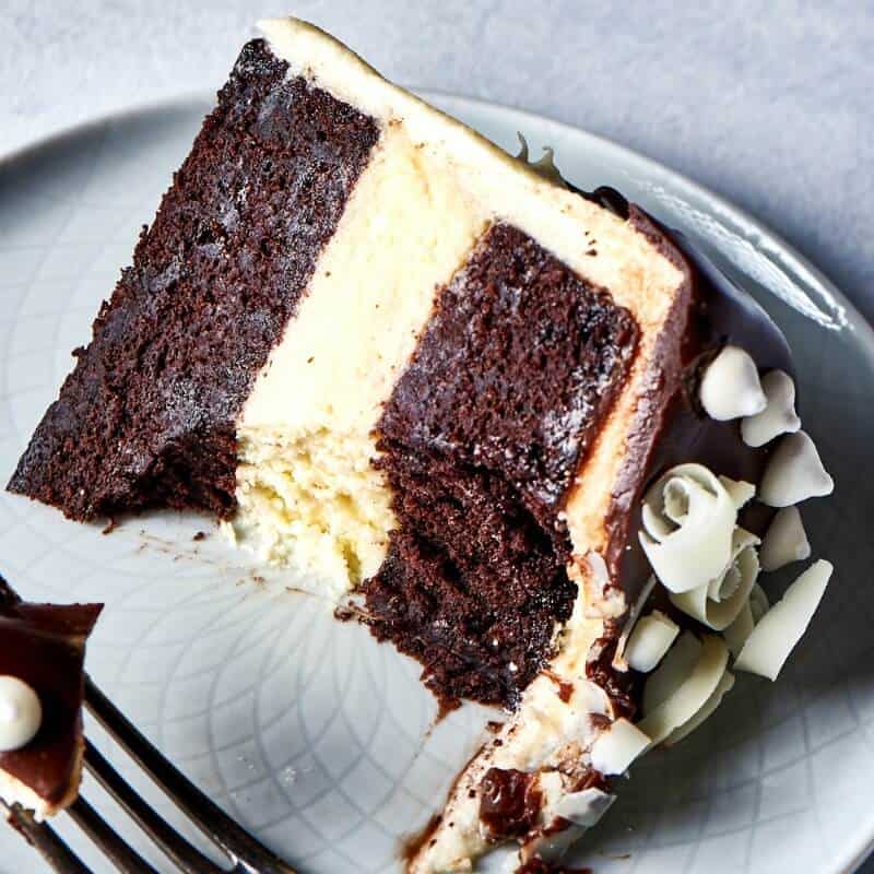 Slice of chocolate cake with cheesecake filling on a white plate with chocolate drizzle