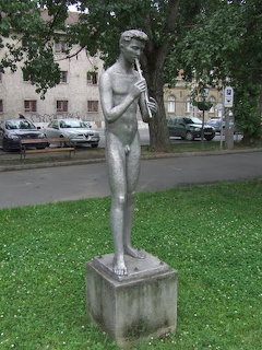 Stone statue of a boy playing flute on pedestal in park