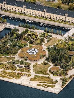 Aerial view of geometric garden with pathways, circular features, trees, and waterfront buildings in Copenhagen