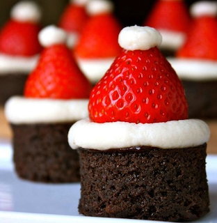 Brownie bites topped with strawberries and white icing like Santa hats