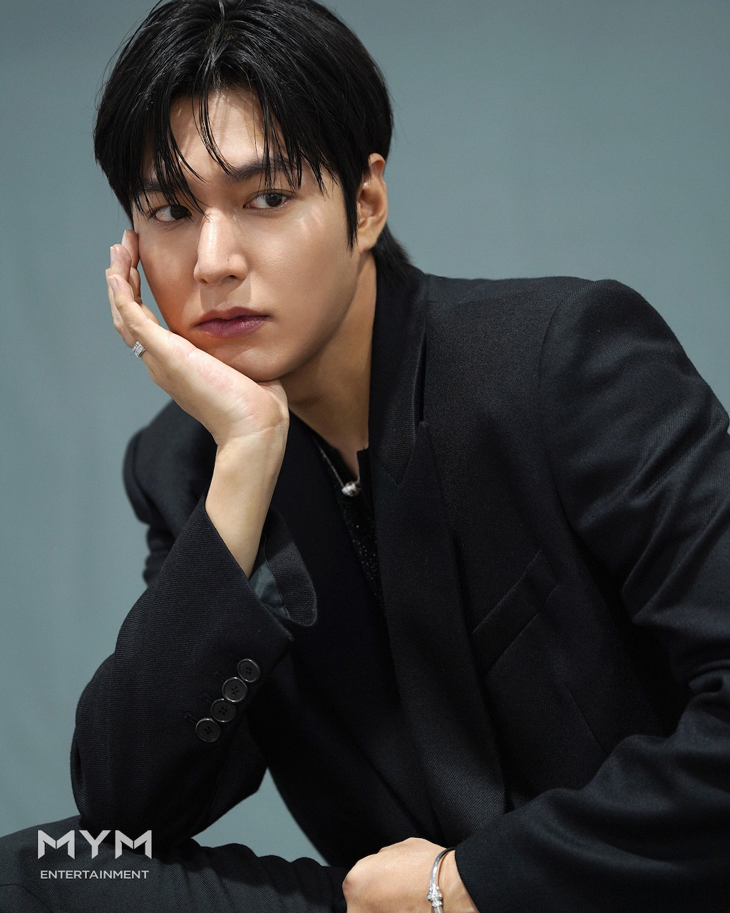 Young Asian man in black blazer posing with hand on cheek in studio portrait